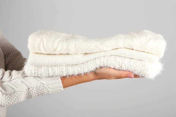 istock Female hands holding folded knitted sweaters on grey background 2205256923