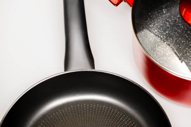 Top-down view of a black non-stick frying pan with a textured bottom and a red cooking pot with a glass lid on a white background. The modern cookware set is designed for home cooking, offering durability and style. Ideal for themes related to cooking, kitchenware, food preparation, and household essentials.