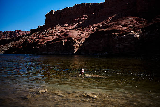 Young woman swimming in river below canyon walls, Lees Ferry, Glen Canyon National Recreation Area,  Arizona.