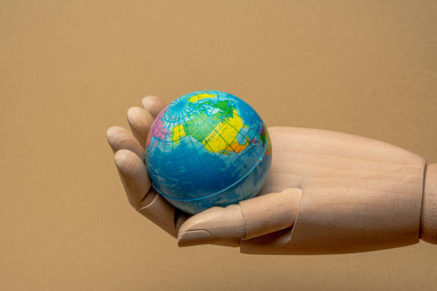 istock Wooden hand holding small globe on beige background 2205282859