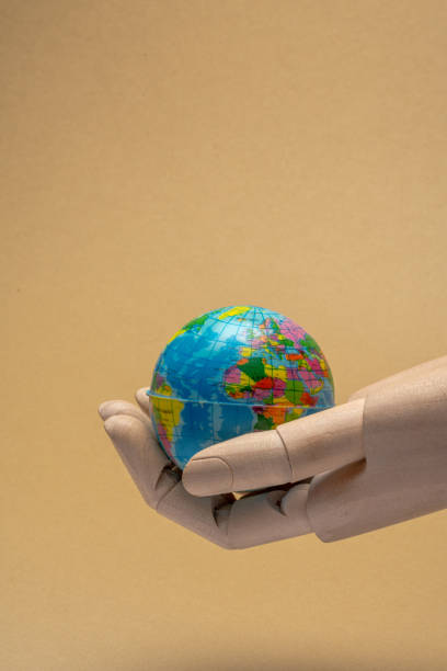 istock Wooden hand holding small globe on beige background 2205282925