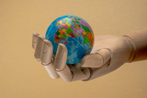 istock Wooden hand holding small globe on beige background 2205282942