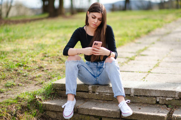 istock Young woman sitting on outdoor steps using her smartphone 2205283133