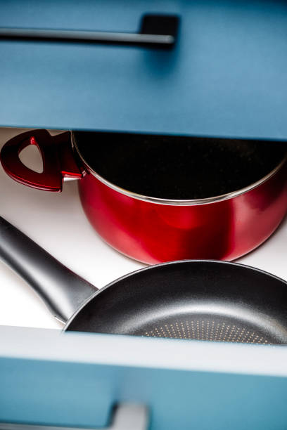 A close-up of a modern red cooking pot with a glass lid and a black non-stick frying pan on a white kitchen countertop. The vibrant red pot contrasts with the sleek black pan, creating a visually appealing kitchen scene. The cookware has a contemporary design, ideal for food preparation, home cooking, and culinary-themed visuals. The image is well-lit, emphasizing textures and materials, making it perfect for content related to home appliances, cookware reviews, and kitchen interiors.