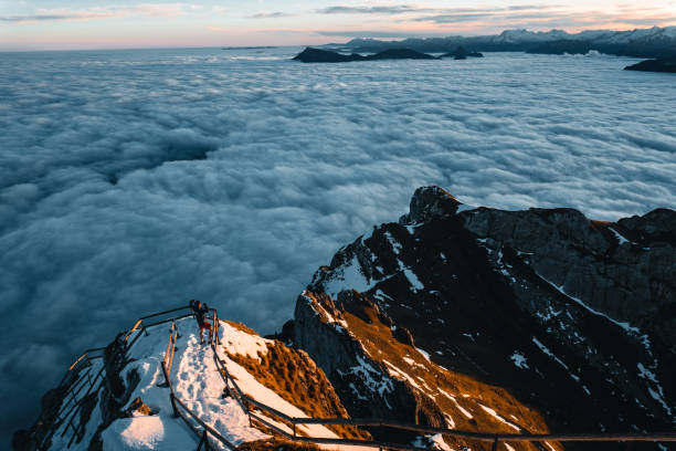 istock Hiker on snowy pathway above clouds and mountains at sunset 2205294362