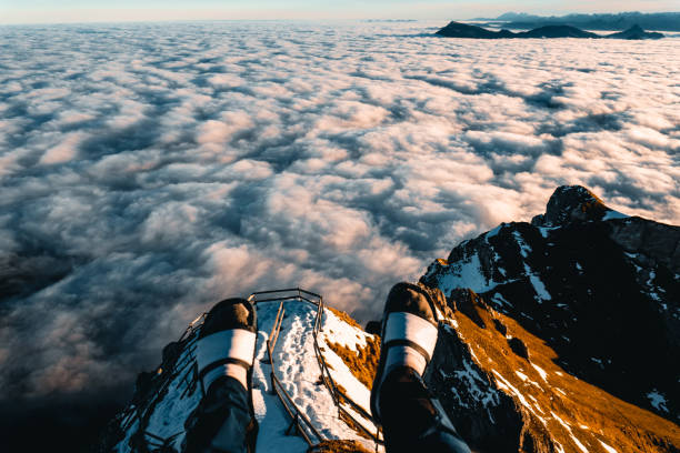 View past hikers feet above cloudscape at dawn, Mount Pilatus viewpoint, Nidwalden Canton, Swiss Alps