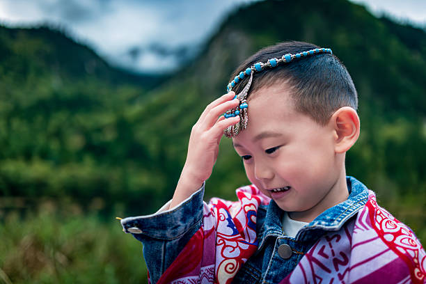A boy stand on a wooden walkway by the lake in Jiuzhaigou. Distant green mountains reflect in the crystal-clear water, with mist swirling around, creating a poetic and picturesque scene