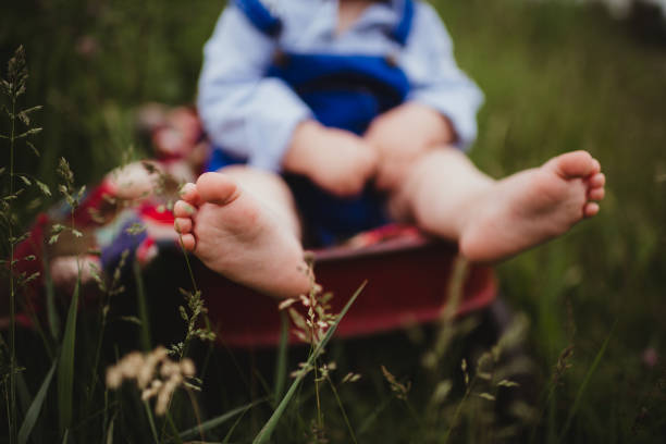 Little toddler boy sitting in red wagon with dirty bare feet and overalls