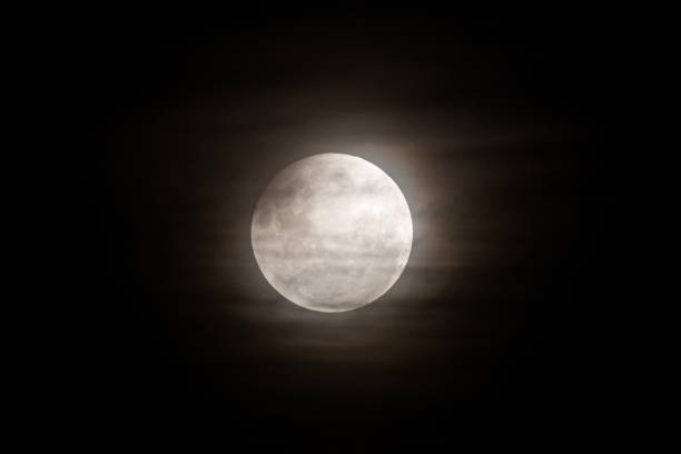 istock A photo of the moon during a partial eclipse, with its top edge slightly darkened and a soft haze from thin clouds diffusing the light 2205308280