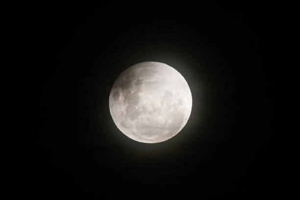 istock A photo of the moon during a partial eclipse, with its top edge slightly darkened and a soft haze from thin clouds diffusing the light 2205308282