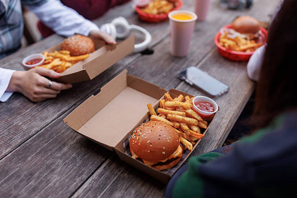 Close up of burger and french fries in box on a table with teenagers sitting around it at fast  food restaurant outdoors