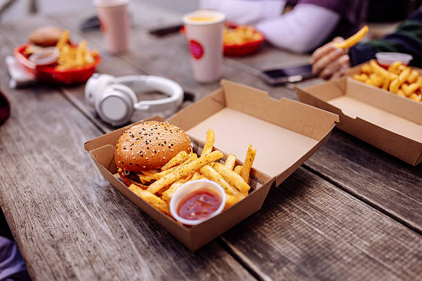 Close up of burger and french fries in a box on a table at street food restaurant with teenagers in a blurry background