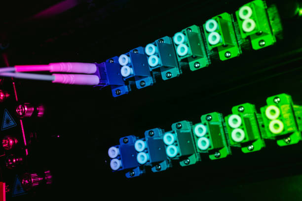 Close-up view of colorful fiber optic connectors reflecting on a dark surface. The vibrant hues create a modern aesthetic, showcasing advanced technology in data transmission.
