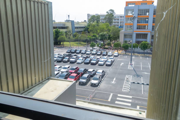 A vibrant urban parking lot scene featuring a variety of vehicles. The view highlights organized parking spaces, modern buildings, and surrounding greenery on a sunny day.