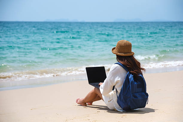 istock A female traveler using and working on laptop computer while sitting on the beach 2205333598