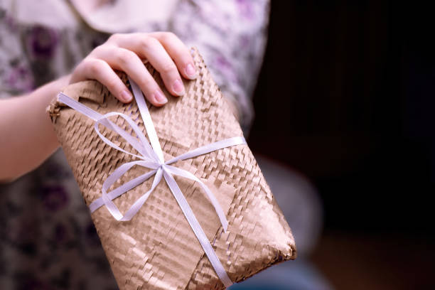 woman's hand presents a rectangular gift wrapped in yellow netted kraft paper, showcasing a thoughtful gesture perfect for any special occasion