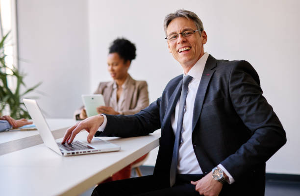 istock Smiling businessman working on laptop in modern office with colleagues 2205341965