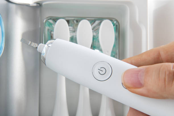 istock Using an electric toothbrush with replaceable attachments  of tooth brush stored in a UV disinfection stand. A hand hold a handle of electric tootbrush. 2205356416