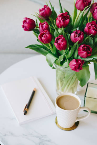 Relaxing purple tulips, coffee mug, notebook, and pen on marble table in the cozy living room