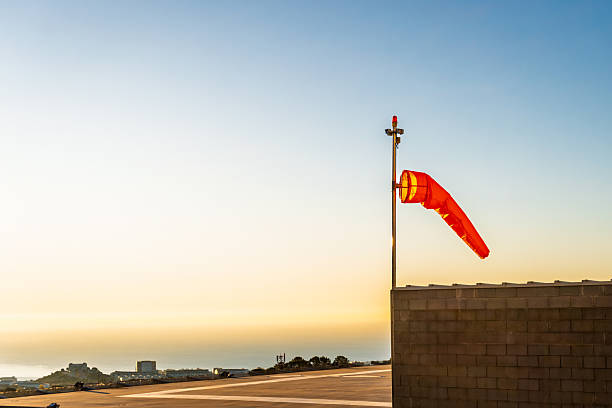 Empty helipad on building roof with windsock indicating wind direction, security camera and antenna during sunset