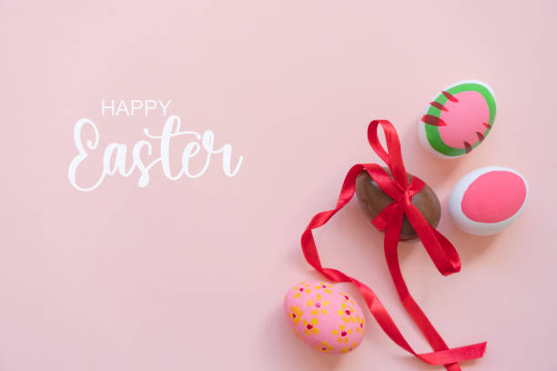 Sweet chocolate egg with bow and painted easter eggs on pink background, top view. Space for text