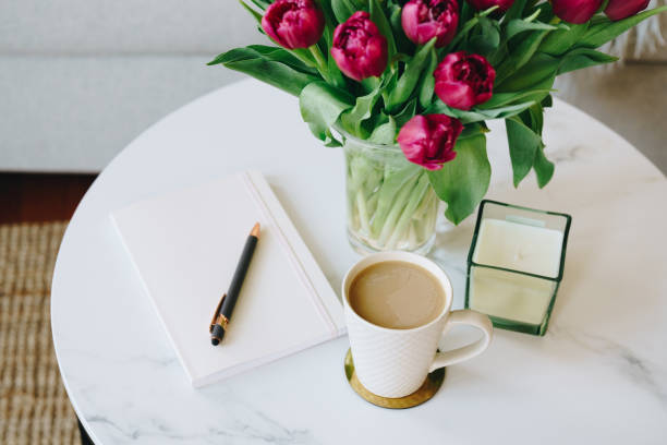 Relaxing purple tulips, coffee mug, notebook, and pen on marble table in the cozy living room
