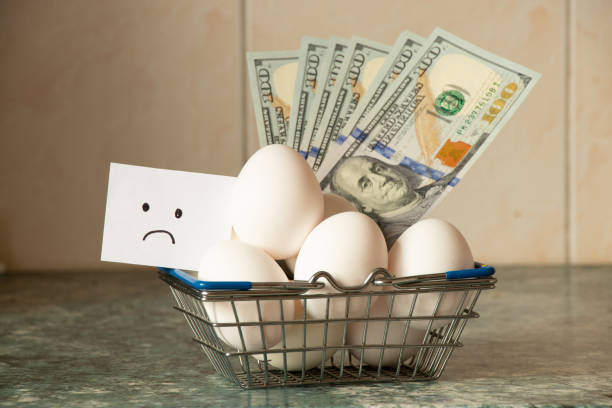 Chicken eggs in a supermarket basket on the table and a sad drawing on paper and dollars in the kitchen, egg shortage stock photo