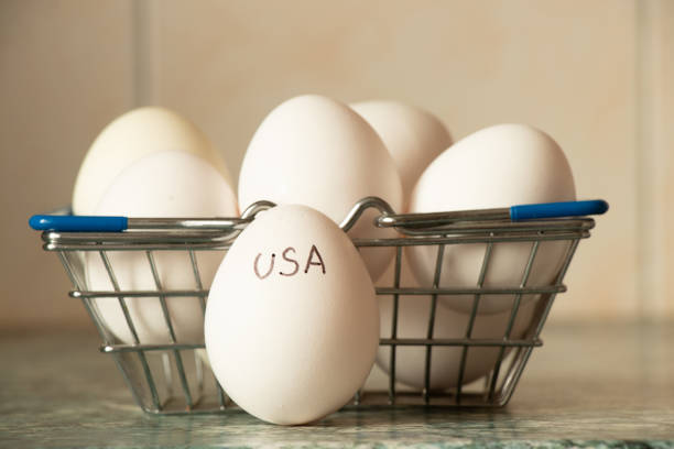 istock Chicken eggs in supermarket basket on table and hand written text USA drawn on egg in kitchen, egg shortage 2205361379