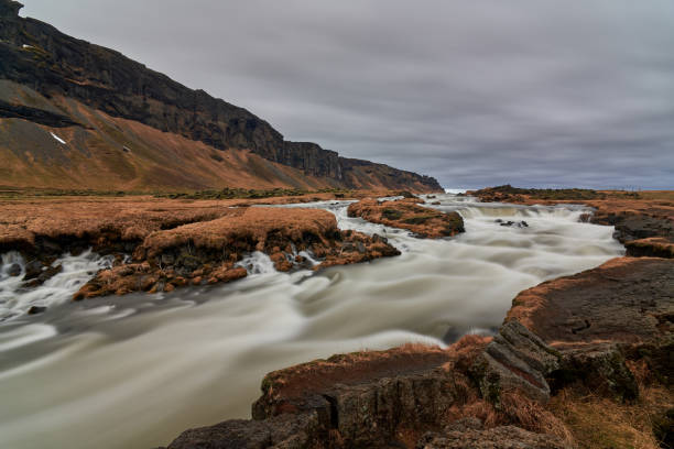 Wide shot of a river flowing through a rocky landscape in iceland with a cloudy sky