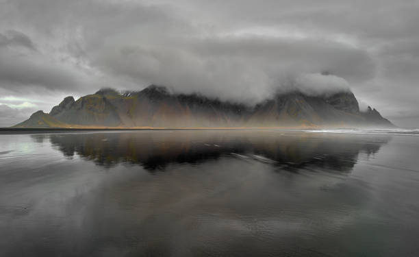 istock Dramatic clouds gathering over Vestrahorn mountain reflecting in water on beach in iceland 2205366157