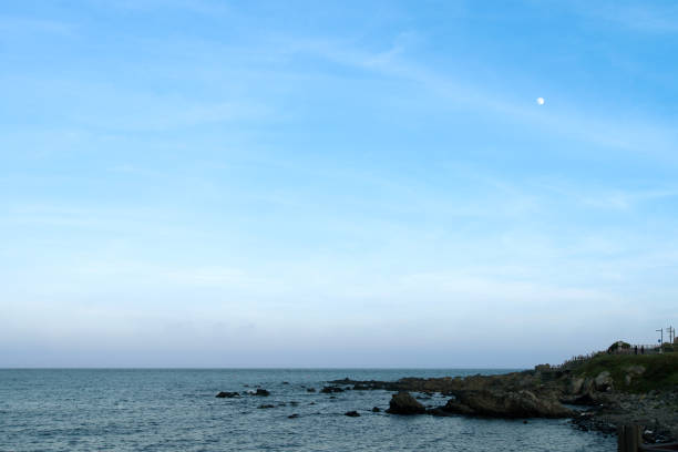 The full moon rises in a starry night sky over the sea and rocky cliffs. The concept of calmness, silence and unity with nature