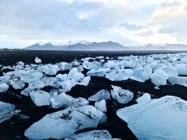 Icebergs lying on black volcanic sand beach in iceland, with mountains and electricity pylons in the background