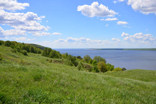 istock Green Hillside Over a Calm River Under a Blue Sky with clouds 2205374828