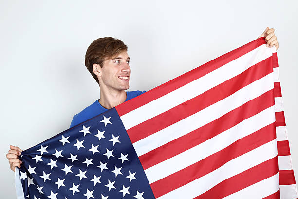 istock Beautiful young man holding an American flag on grey background 2205375281
