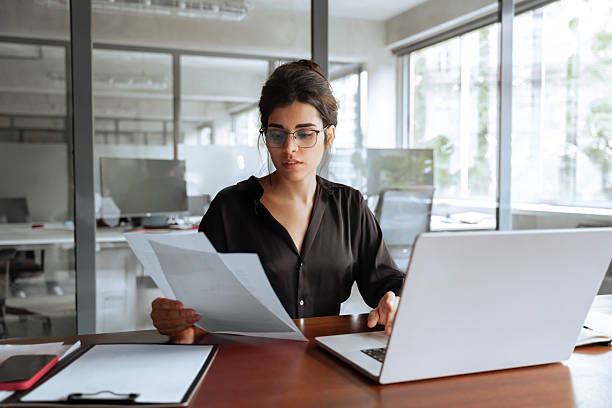 istock Latin business woman accountant holding documents, working at laptop pc computer doing online tax invoice, financial report. Focused Hispanic businesswoman manager specialist with paperwork in office 2205384541