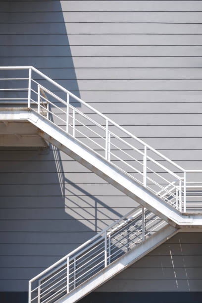 White metal fire escape on gray industrial office building wall background in vertical frame