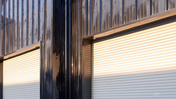 istock Two automatic white roller shutter entrance doors on black corrugated metal wall of modern building in industrial minimal style with light and shadow on surface 2205386136