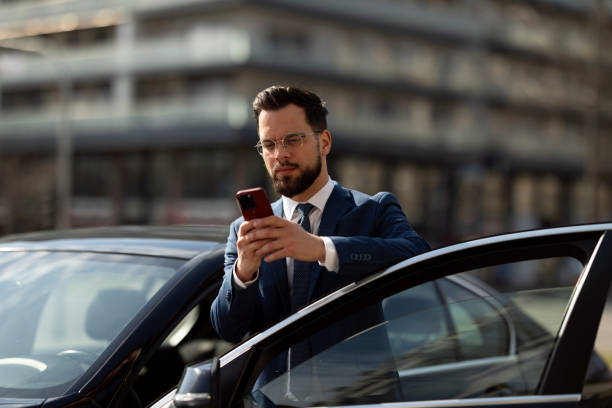 istock Businessman Checking Smartphone Beside CarDescription: 2205387567