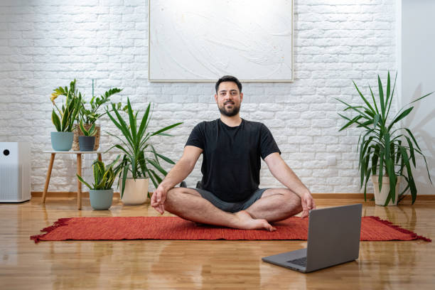 istock Man Practicing Yoga At Home With Laptop And Indoor Plants 2205391312