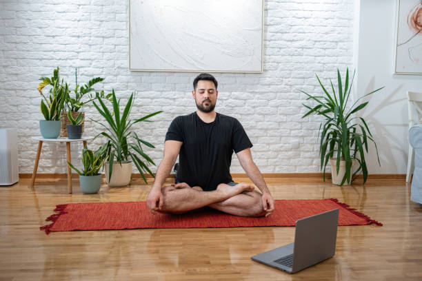 istock Man Practicing Yoga Meditation at Home Using a Laptop 2205391328