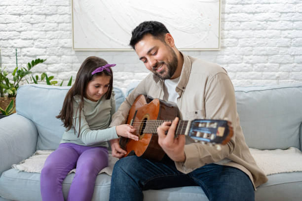 istock Father teaching daughter playing guitar on couch at home with joy 2205392349