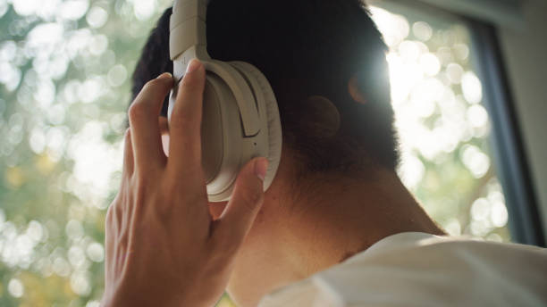 Asian young man wearing headphones while looking through the window.