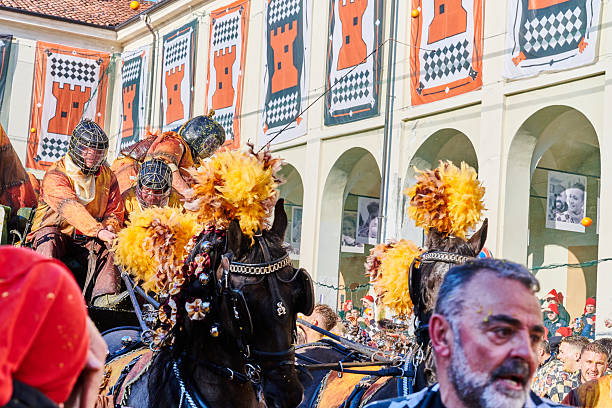 Ivrea, Italy - March 02, 2025: groups in traditional dressing ride a cart pulled by horses during the Battle of the Oranges. The team \