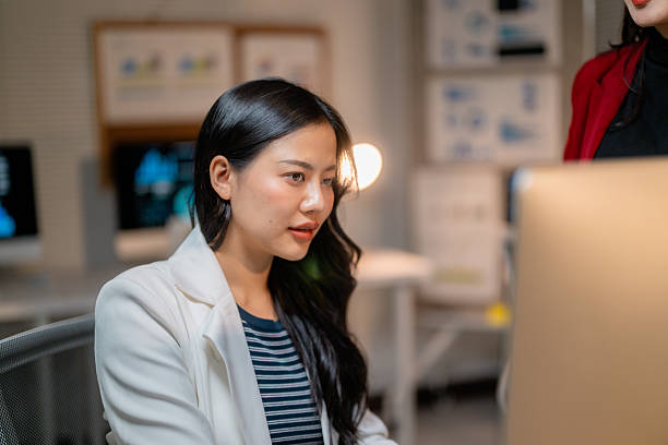 istock Two young Asian businesswomen discussing work together using laptop computer in modern office 2205400690