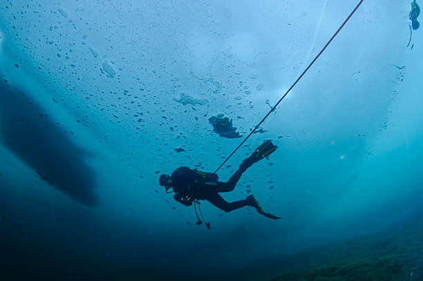 Scuba diver gliding under frozen lake surface in Panticosa, Spain, navigating icy underwater environment with specialized diving gear and professional technique