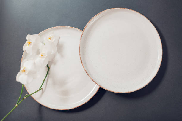 istock Top view of glazed ceramic dishware on grey background. Set of white speckled dinner plates orchid flowers 2205404174