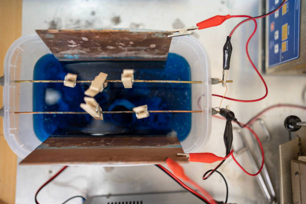 Close-up overhead shot of an electrochemical experiment showcasing metallic electrodes, a blue electrolyte solution, and electrical connections within a controlled laboratory setup for scientific purposes.