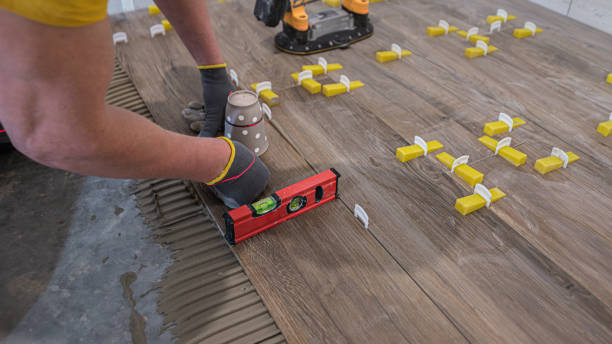 istock Tiling work a floor in the bathroom.  A tiler's hands aligns the tile to horizontality. Checks it with a spirit level and a laser. 2205412018