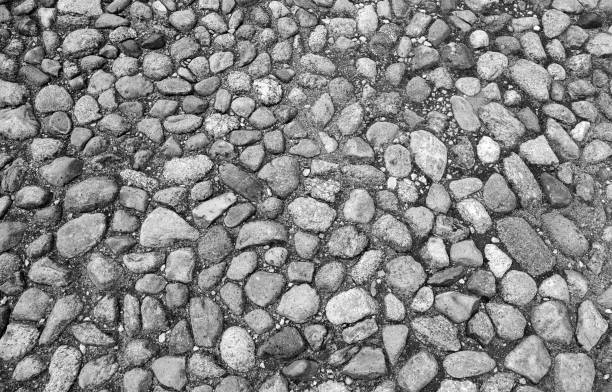 Vintage road pavement with gray round granite stones in ground, top view, background texture. Black and white photo