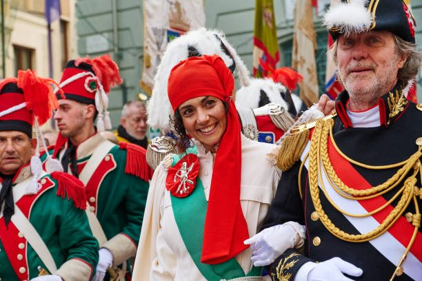 Ivrea, Italy - March 02, 2025: a young woman with the mugnaia (Miller's Daughter) costume at Ivrea Carnival. She is the symbol of freedom and the heroine of the festival since her appearance in 1858. She is parading though the city accompained by the General. According to legend, the brave maiden liberated the people from tyranny by killing the Marquis of Monferrato, who starved the city and forced young brides to the ius primae noctis. The miller first seduced the nobleman, then she rebelled on the night of the encounter, cutting off his head with his own sword and initiating the popular uprising.